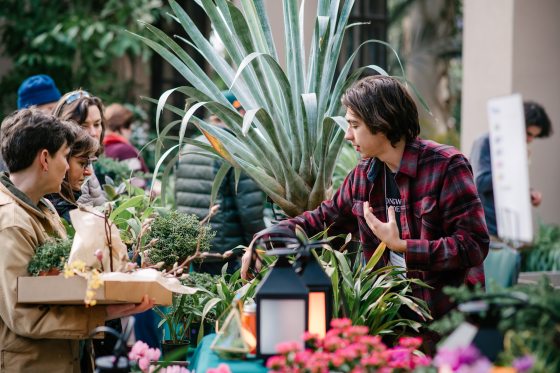 a person selling plants behind a table with people paying 